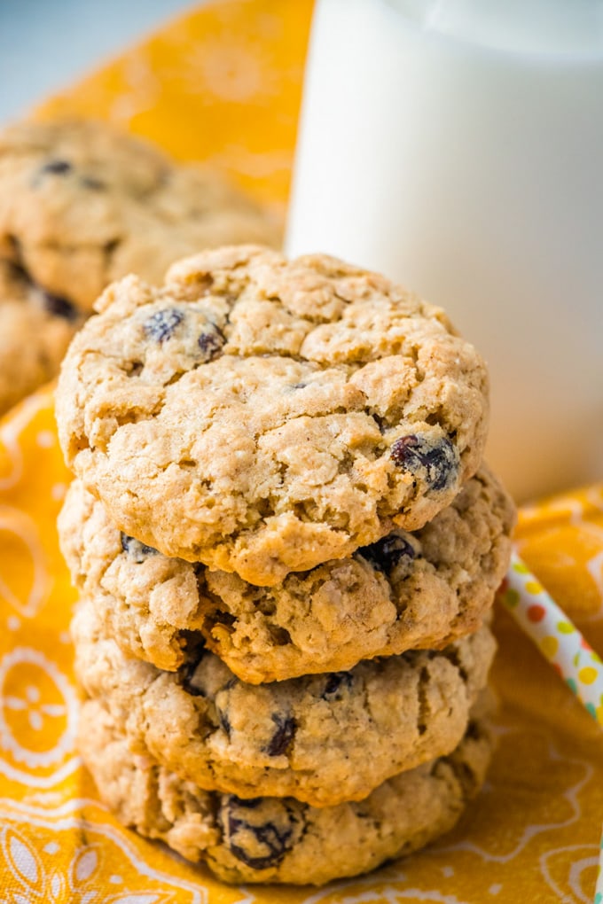 A stack of Oatmeal Raisin Cookies, a glass of milk and a yellow napkin.