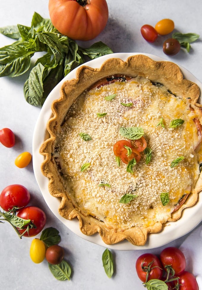 An overhead shot of a classic tomato pie surrounded by lots of fresh tomatoes.