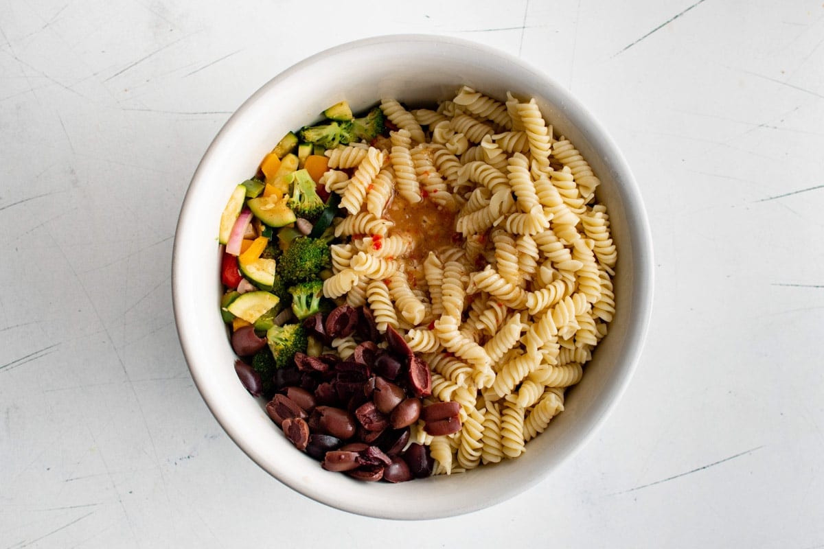 Rotini, kalamata olives, vegetables in a white bowl with Italian dressing.