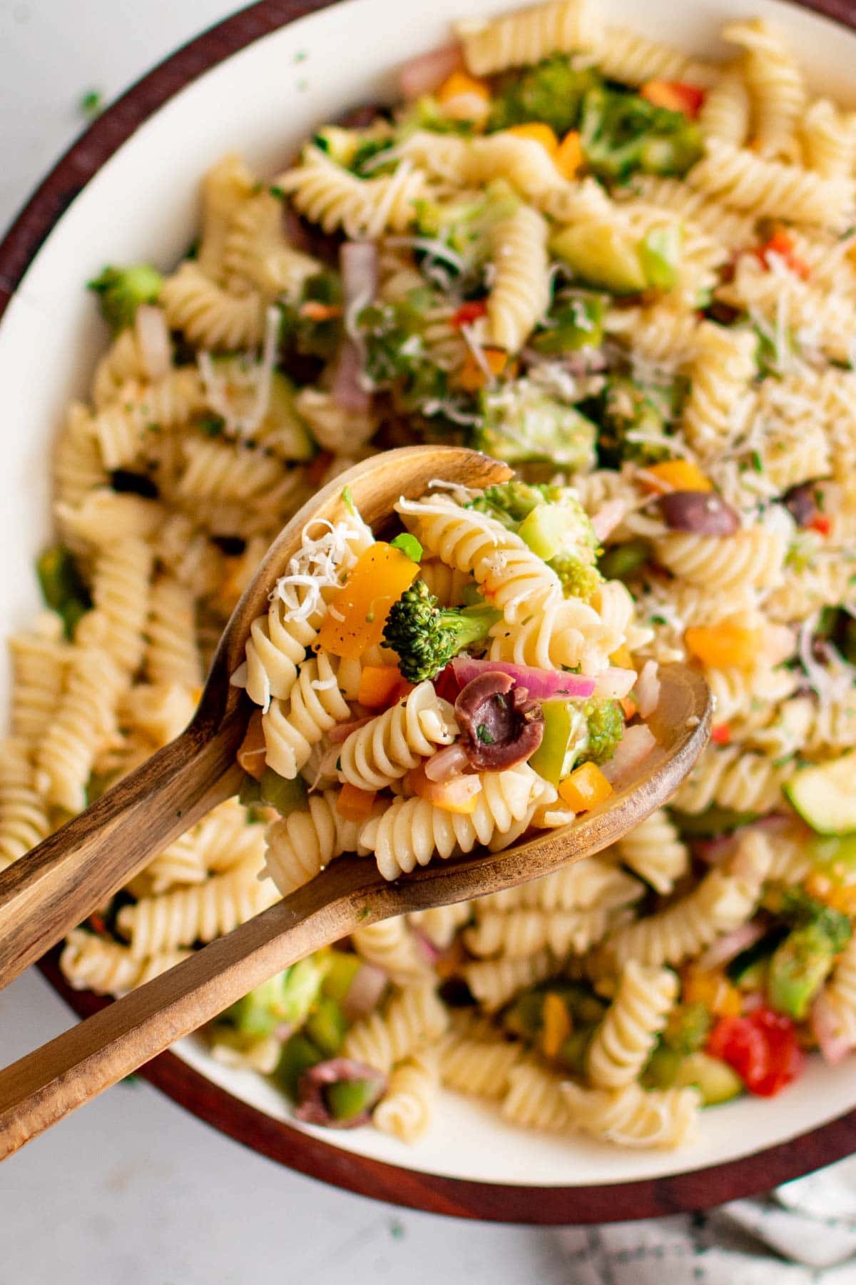 Salad tongs holding a serving of pasta salad with vegetables.