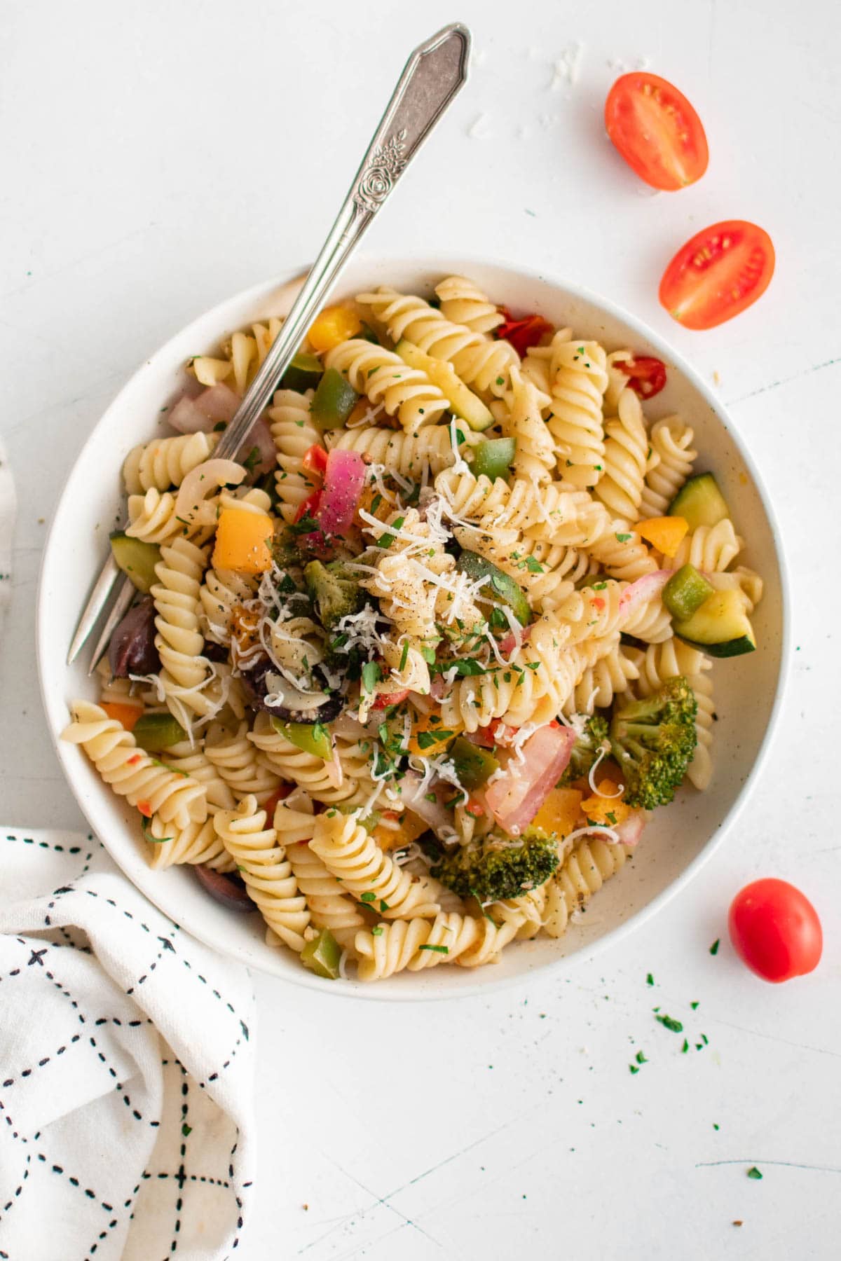 Rotini, vegetables, parmesan cheese in a small bowl with a fork.