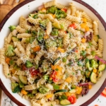 Rotini pasta and vegetables with parmesan cheese on top in a large glass bowl.