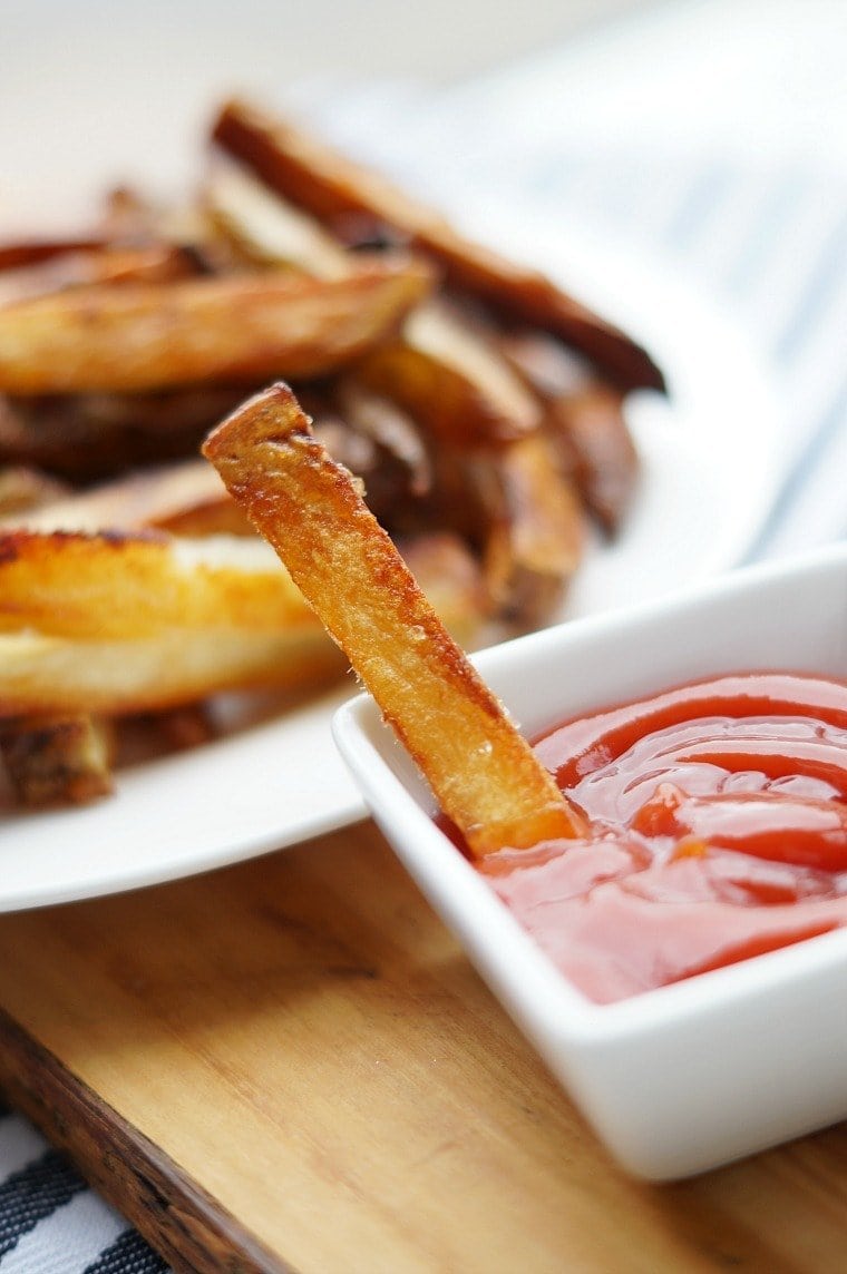 A crispy oven baked french fry sitting in a bowl of ketchup.