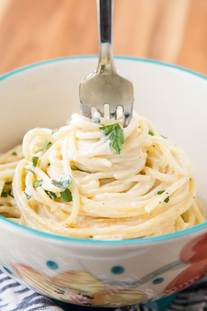 This Four Cheese Spaghetti is ultra creamy and garlicky. It comes together in under 20 minutes, making it a perfect weeknight meal. Four cheese spaghetti pasta in a bowl twirled by a fork