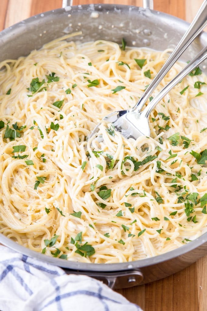 This Four Cheese Spaghetti is ultra creamy and garlicky. It comes together in under 20 minutes, making it a perfect weeknight meal. A skillet of 4 cheese spaghetti with a spoon and fork.