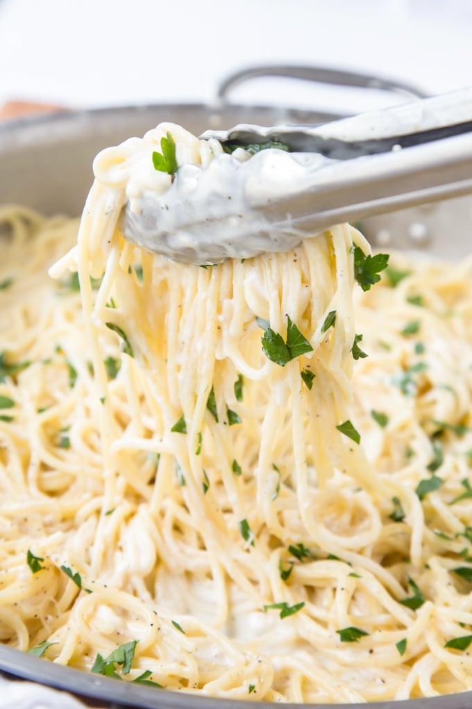 A helping of 4 cheese spaghetti being lifted out of the pan with tongs.