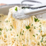 Cheese sauced spaghetti with metal tongs.