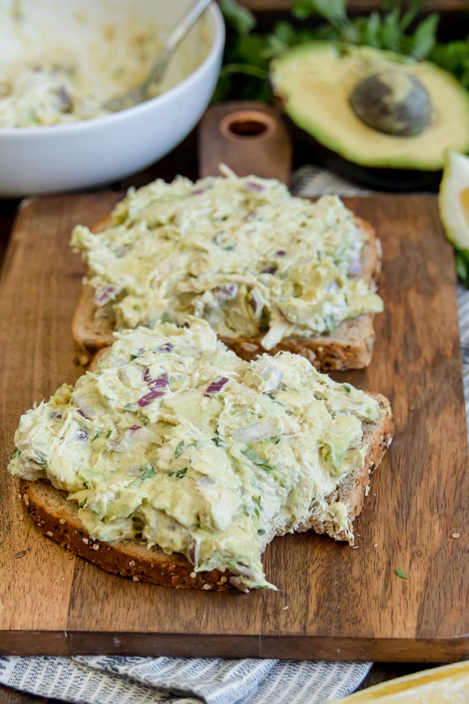 Avocado chicken salad on sliced bread with a bite taken out of one slice.