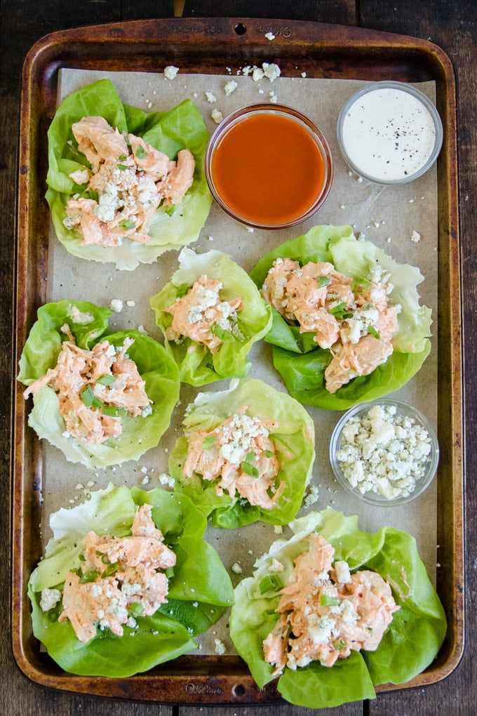 A tray filled with buffalo chicken salad lettuce wrqps and small bowls of ranch and buffalo sauce.