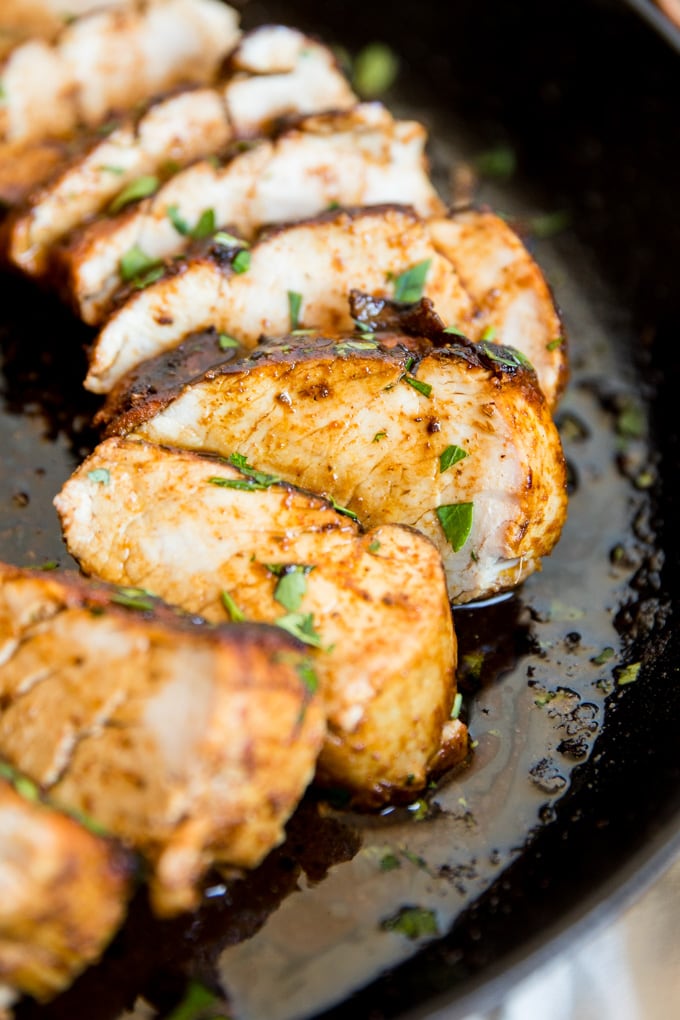 A close up o a sliced pork tenderloin with juices over it.