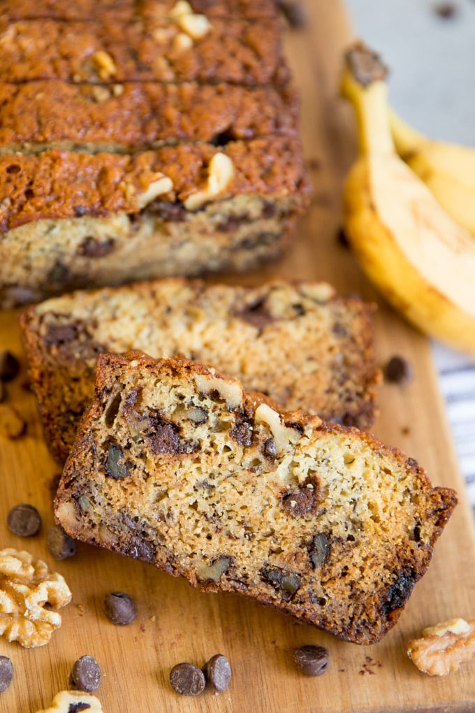 A slice of chunky monkey banana bread surrounded by walnuts and chocolate chips.