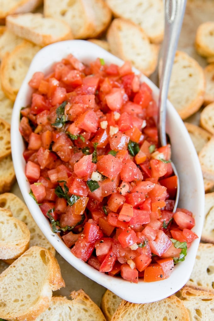 A bowl of bruschetta mixture surrounded by toasted bread