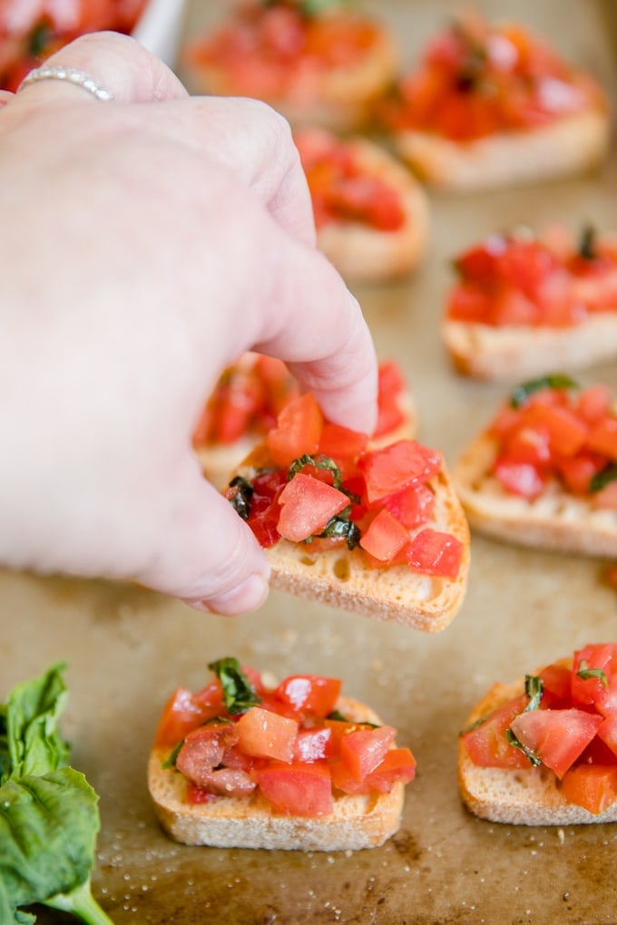 a hand reaching in to grab a piece of tomato bruschetta