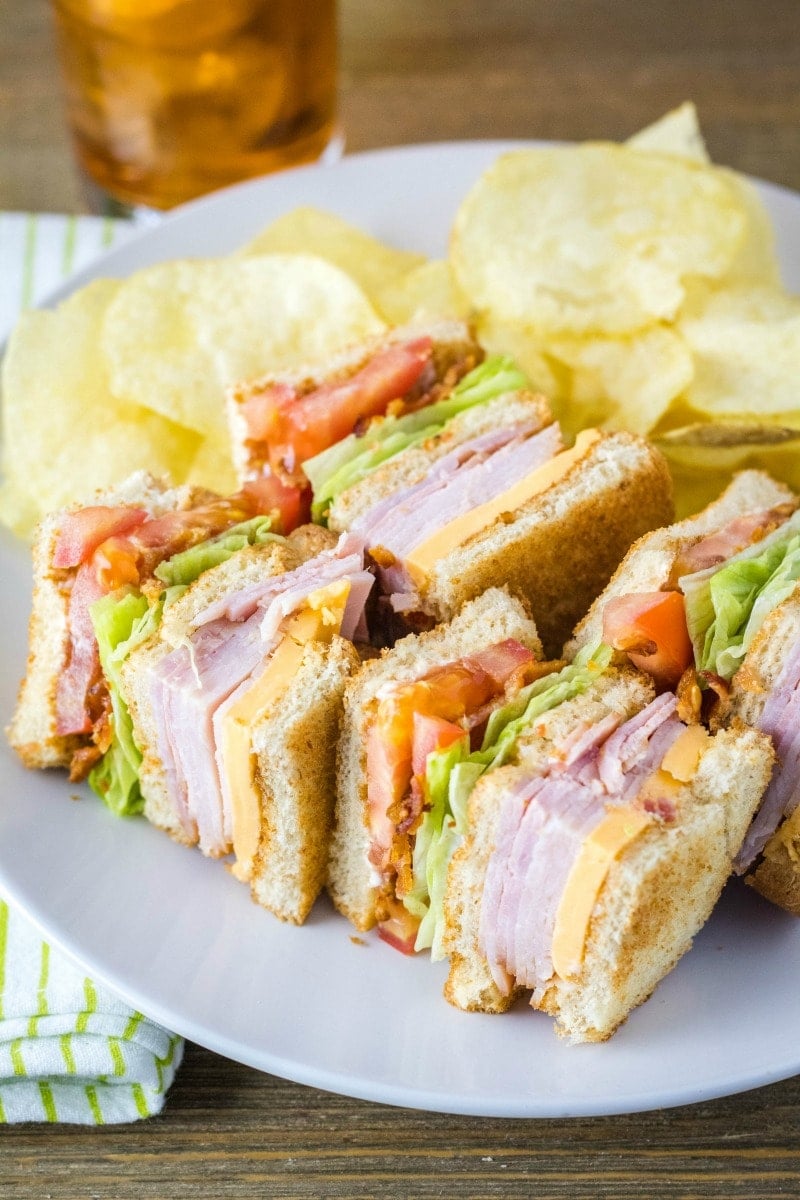 clube sandwich cut into quarters, laying down on a plate with chips