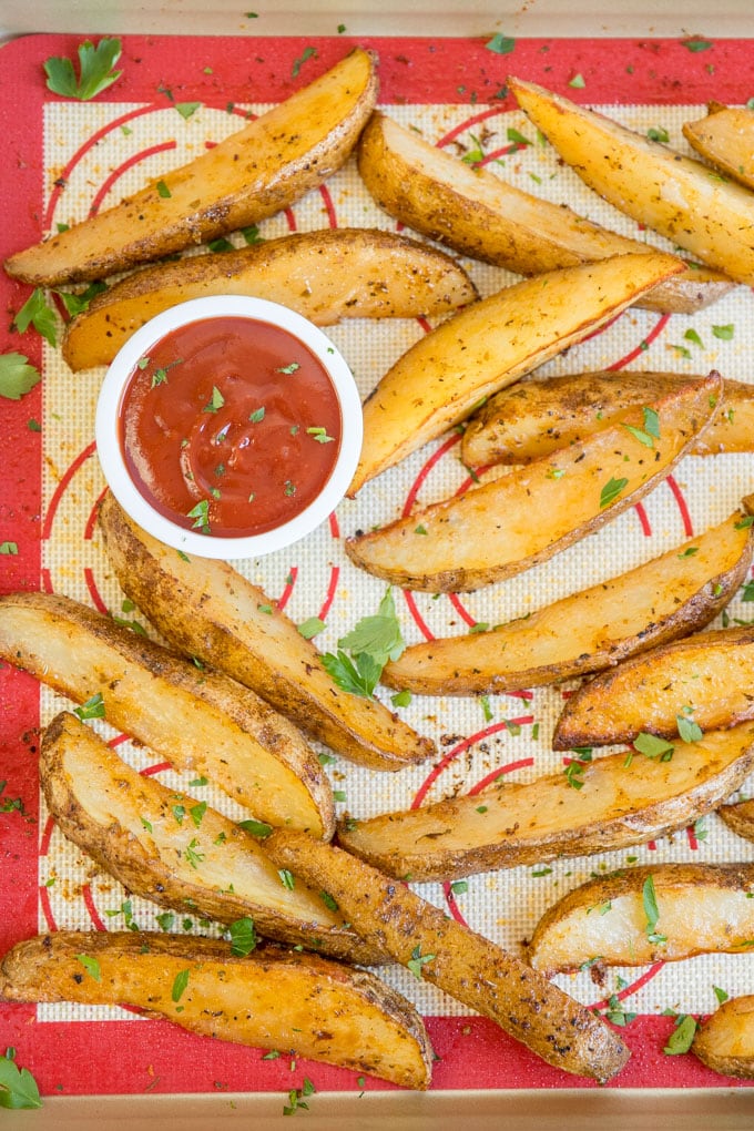baked potato wedges arranged on a silicone mat on a baking sheet.