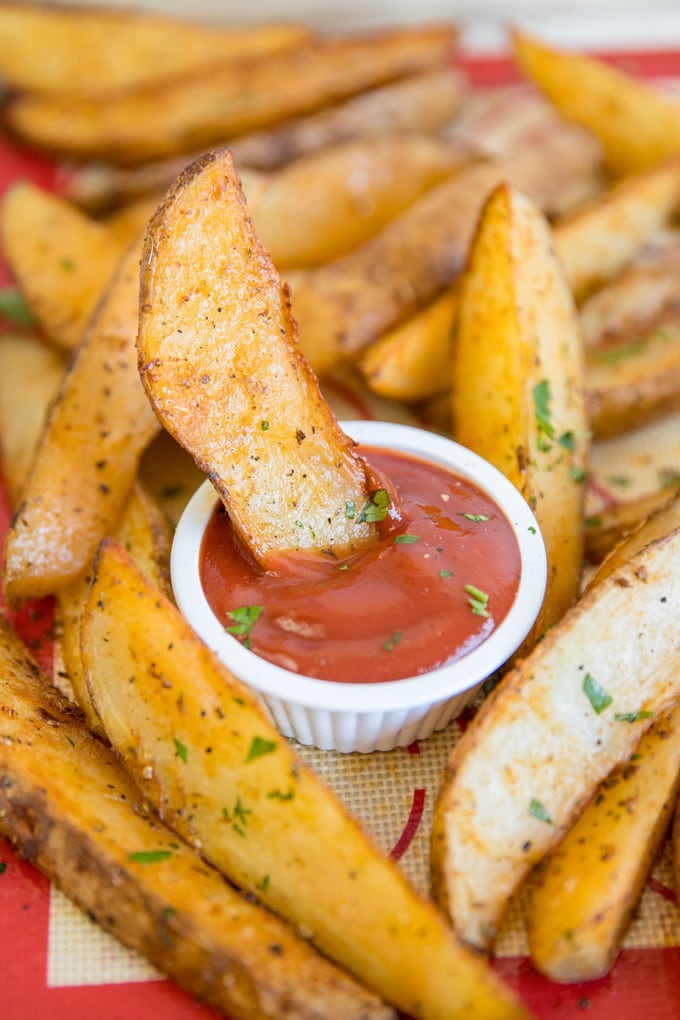 baked potato wedges, with one sitting in a dish of ketchup.