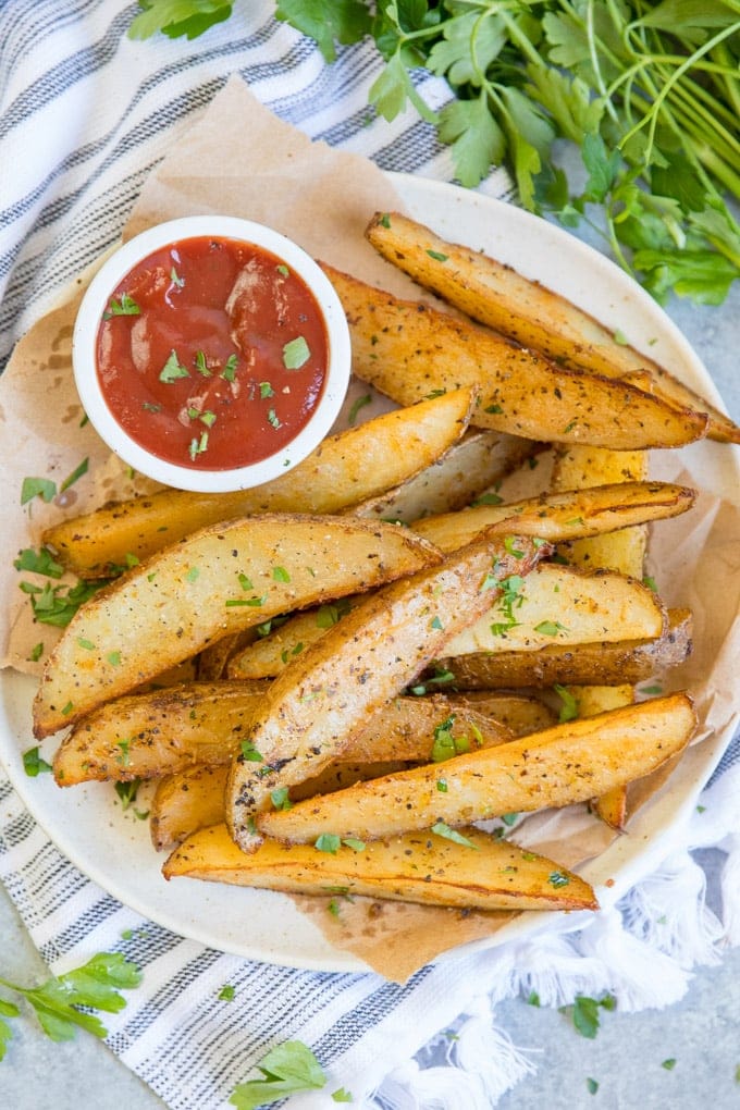 baked potato wedges on a white plate with a dish of ketchup.