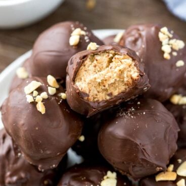 A plate of peanut butter balls stacked in a pyramid with one peanut butter ball with a bite taken out of it.