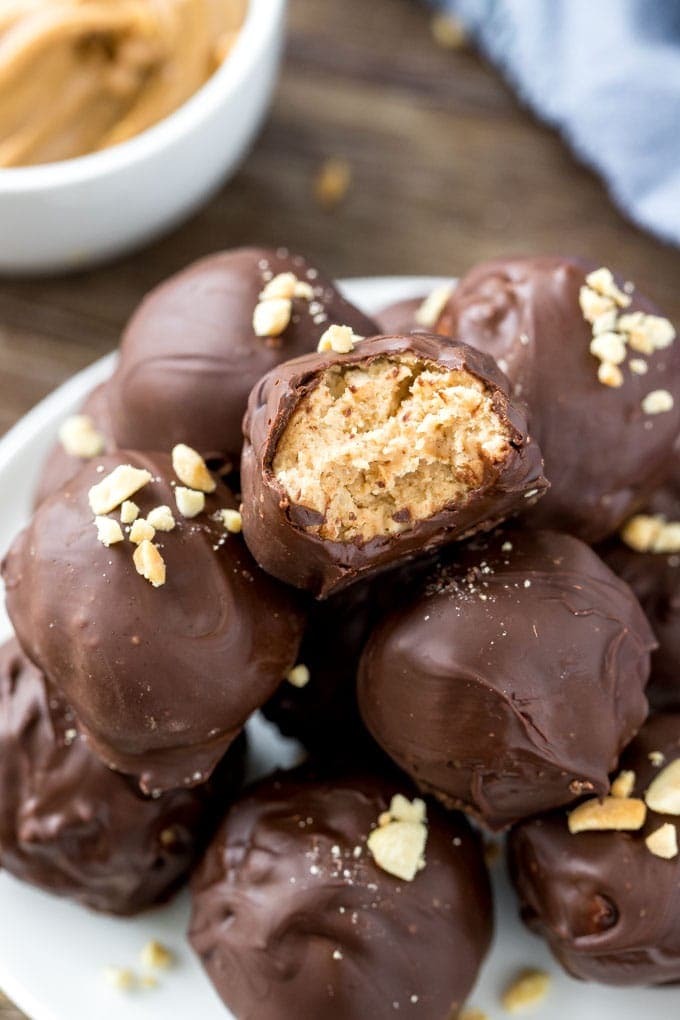 A plate of peanut butter balls stacked in a pyramid with one peanut butter ball with a bite taken out of it.