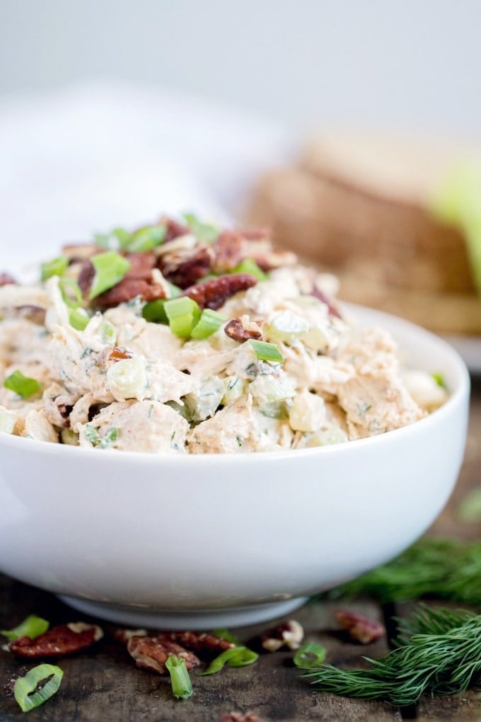 A bowl of chicken salad with dill and topped with pecans and green onions.