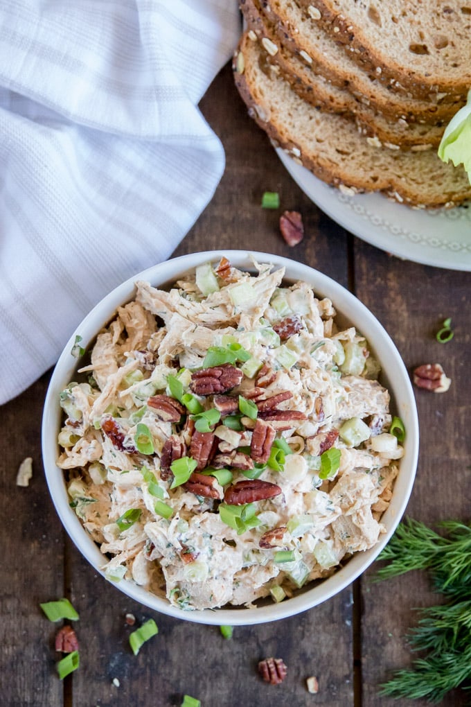 An overhead shot of chicken salad in a bowl on a wood background, with slices of wheat bread and lettuce.