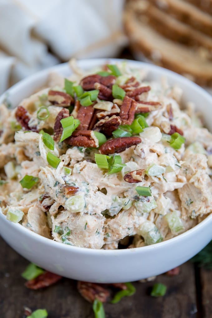 Chicken salad in a white bowl topped with pecans and onions
