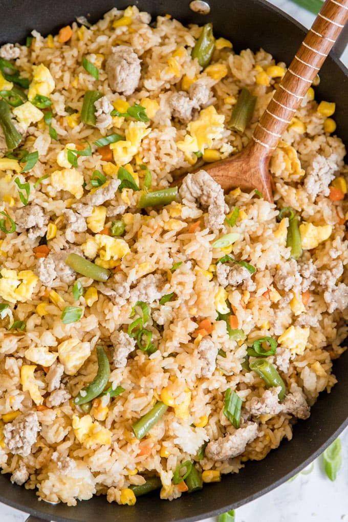 An overhead shot of a skillet full of pork fried rice, with a wooden spoon in it.