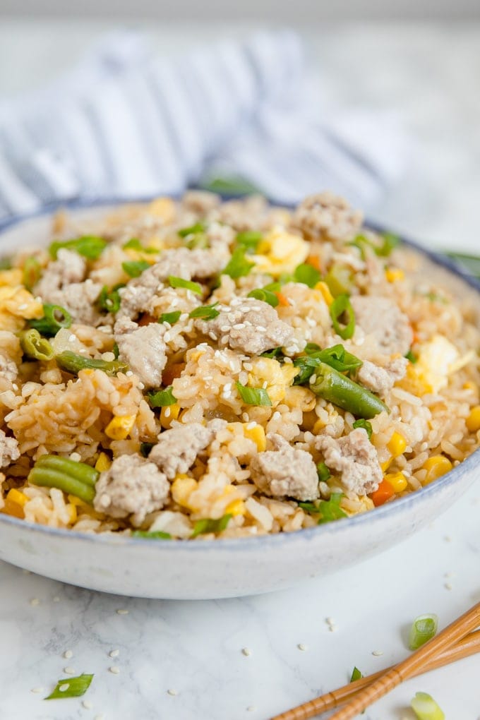A bowl with pork fried rice topped with sesame seeds and sliced green onions.
