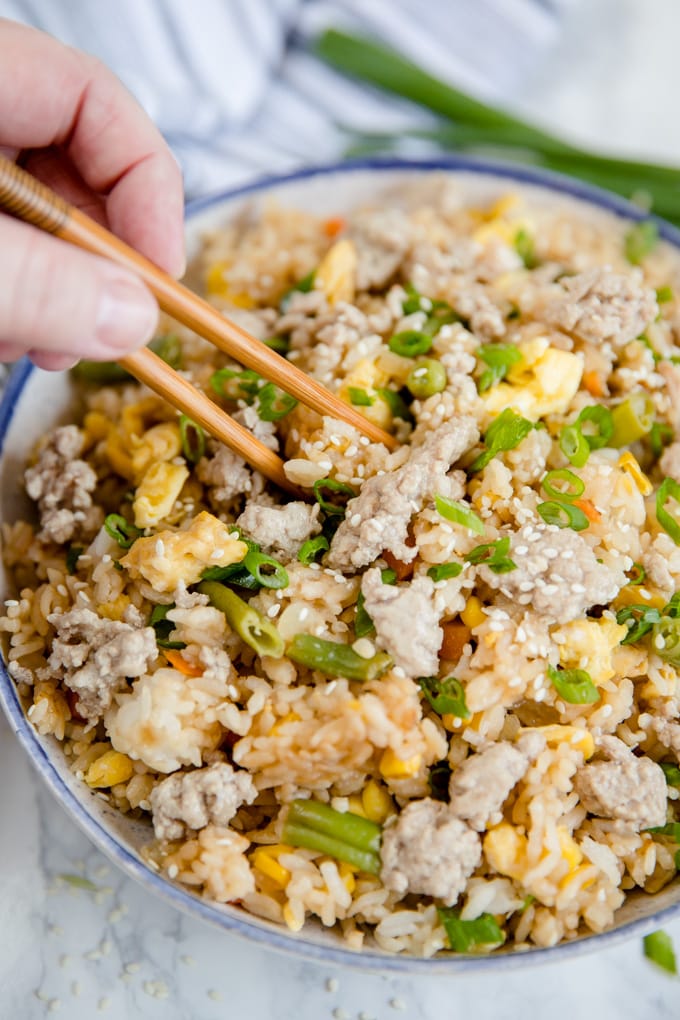 Pork Fried Rice in a bowl and a hand reaching in to take a bite with chopsticks.