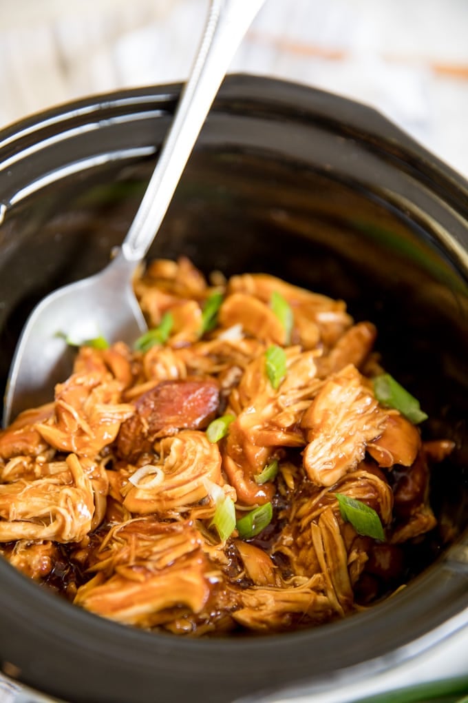 Crock pot teriyaki chicken in a slow cooker with a silver spoon.