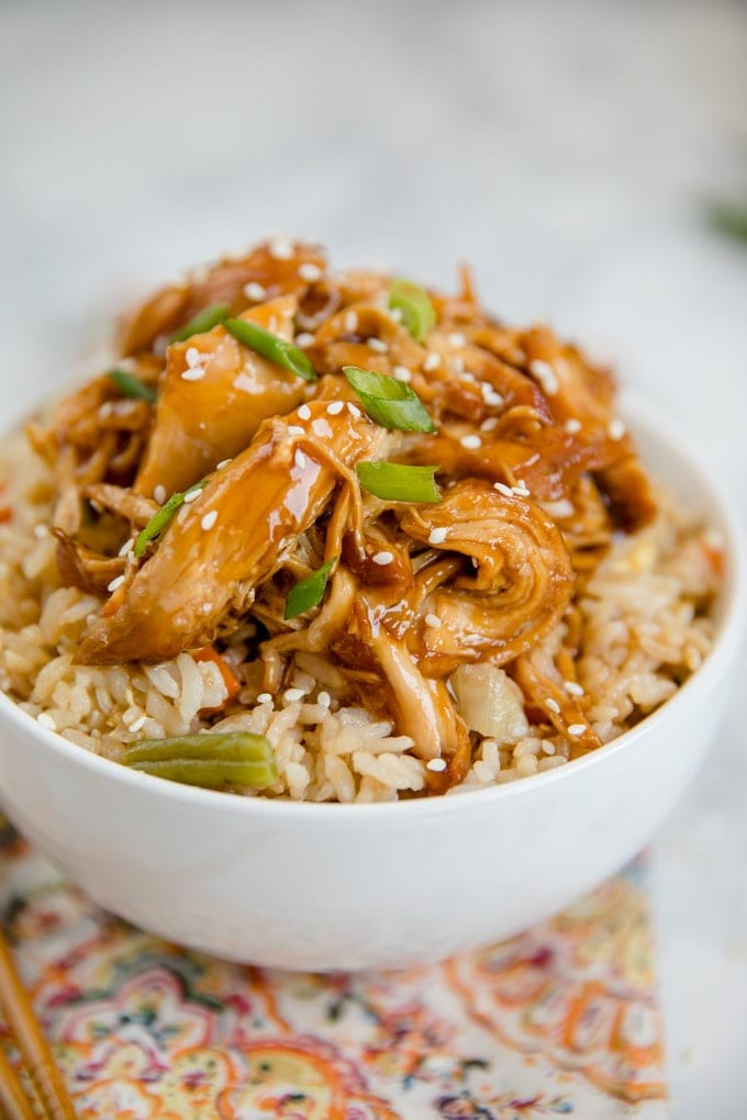 Crock pot teriyaki chicken in a white bowl over a bed of fried rice.