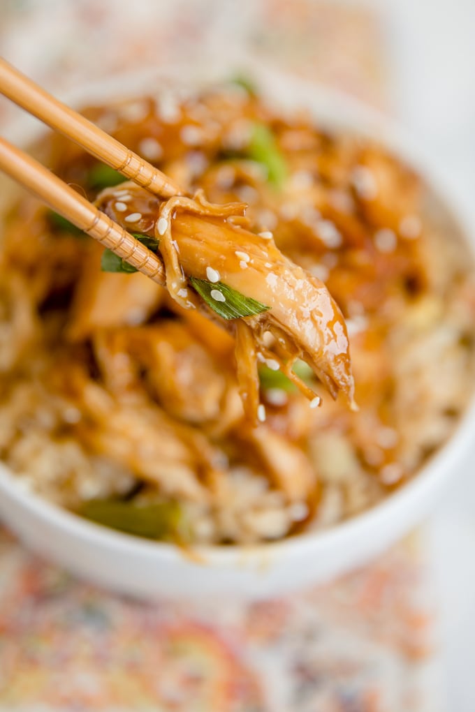 A piece of teriyaki chicken held between two chopsticks.