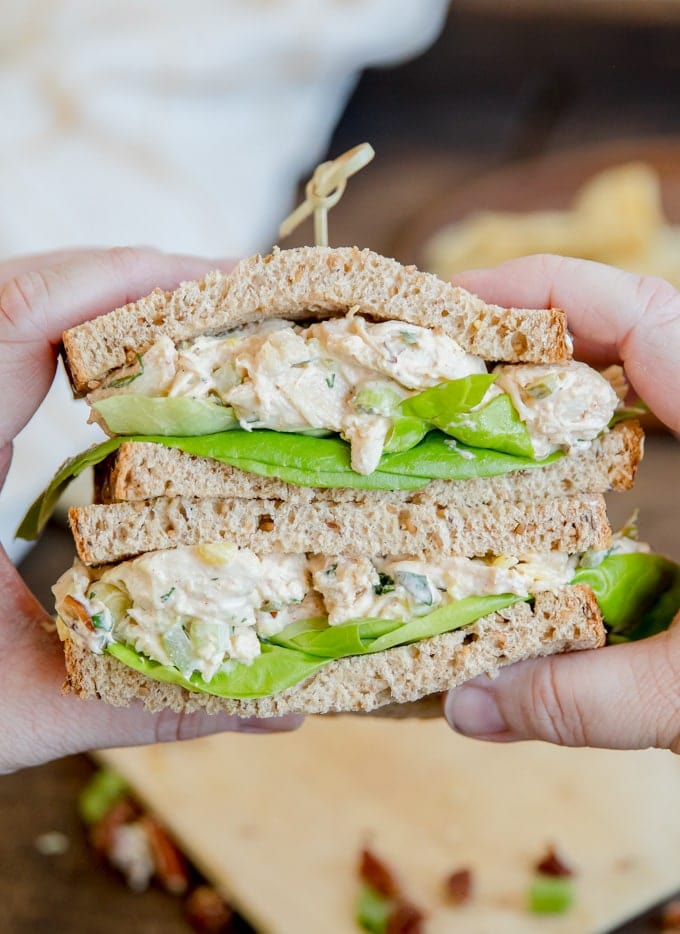 Hands holding two stacked halves of a chicken salad sandwich.