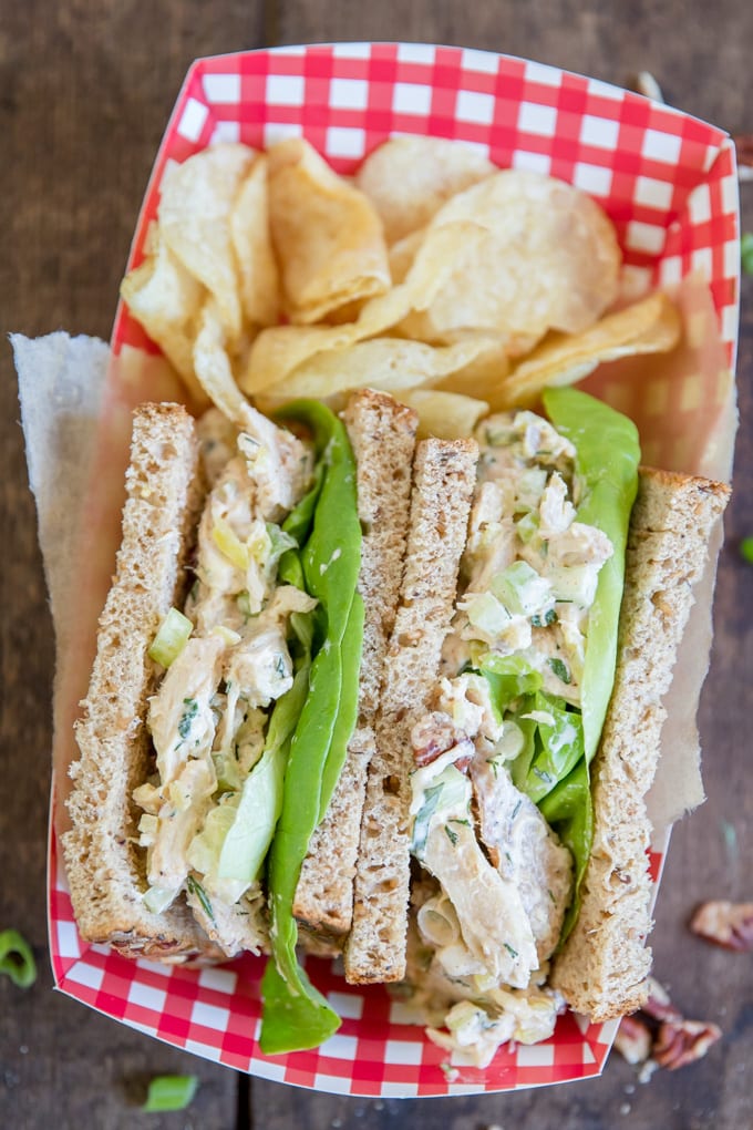 Two halved of a chicken salad sandwich face up in a red gingham container.
