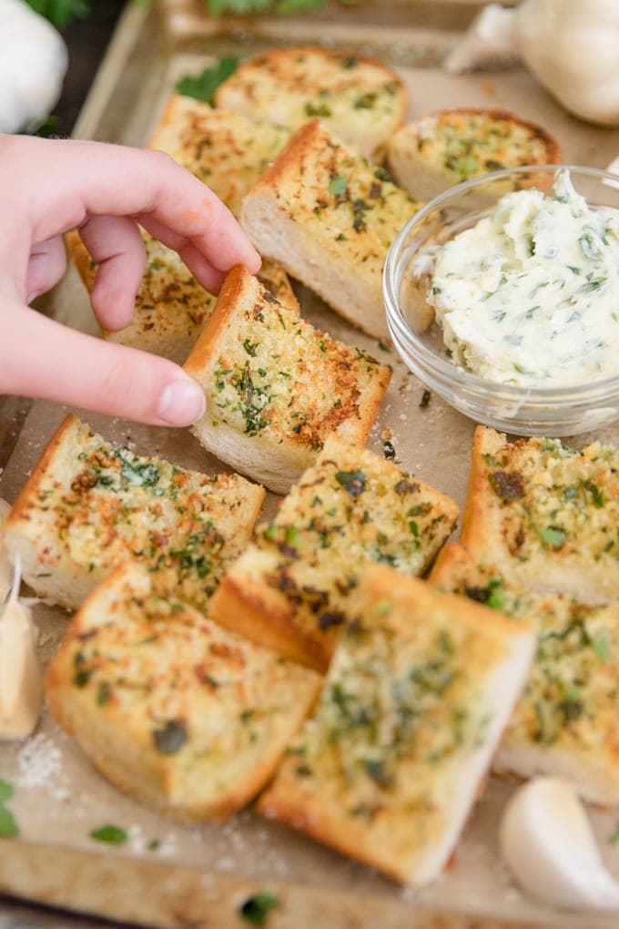a little hand reaching in to grab a slice of garlic bread