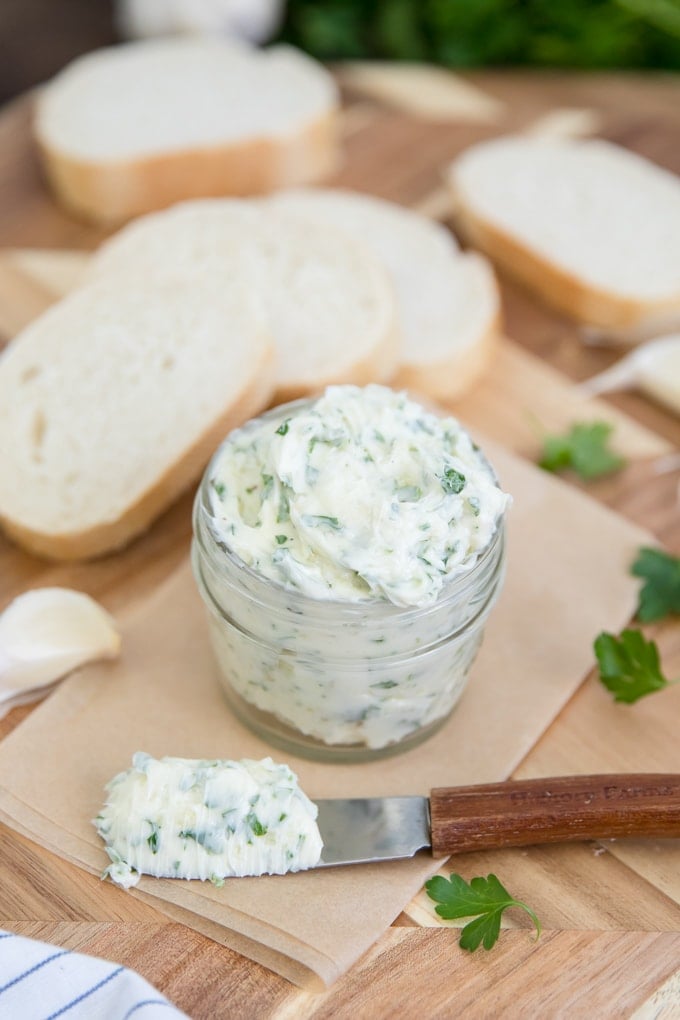 homemade garlic butter in a jar and on a knife surrounded by sliced bread
