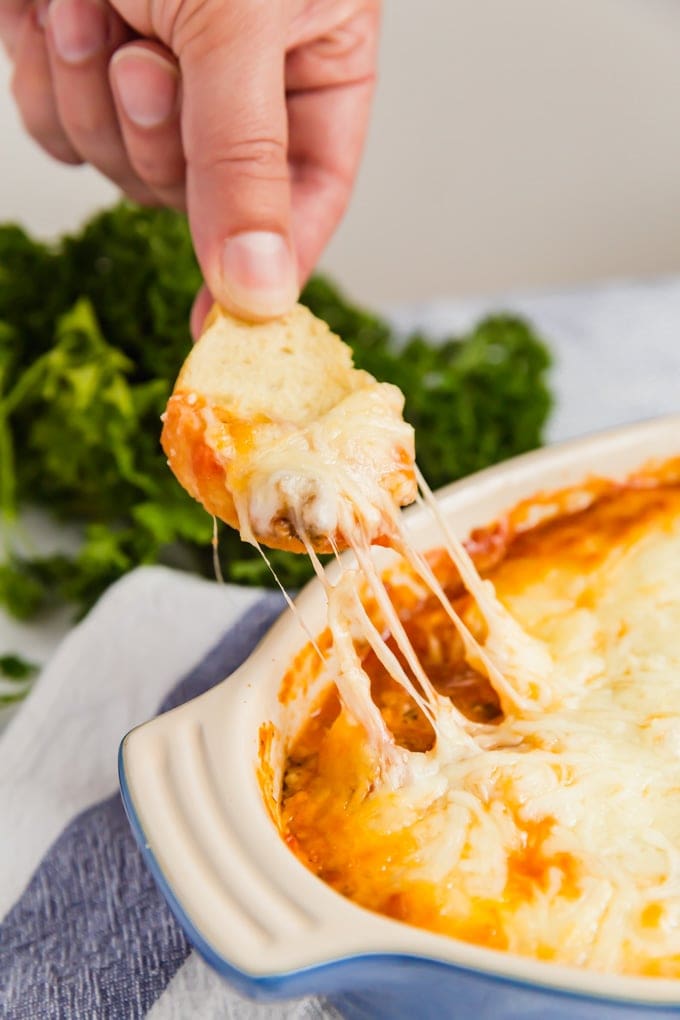 A hand pulling a sliced baguette with melted cheese from a dish of Lasagna Dip