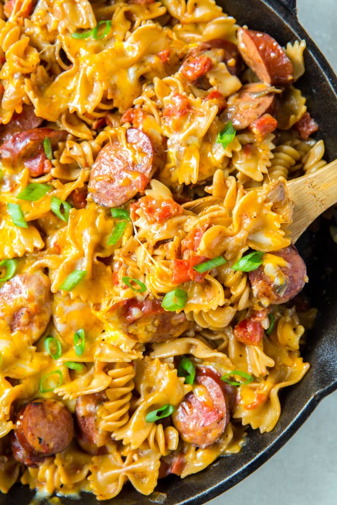 Cheesy Sausage Pasta with a creamy sauce in a skillet with a wooden spoon