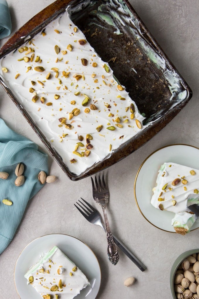 An overhead shot of pistachio pudding cake in a pan with slices on plates.