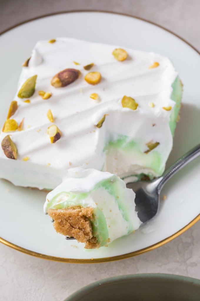 A close up of a slice of pistachio cake with a bite on a fork