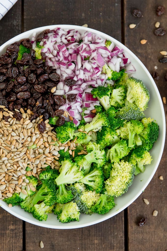 Broccoli, red onions, sunflower seeds and raisins in a bowl ready to make broccoli salad