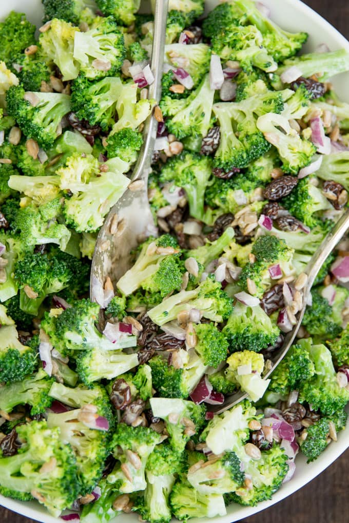 An overhead close up image of broccoli salad with two spoons in a bowl