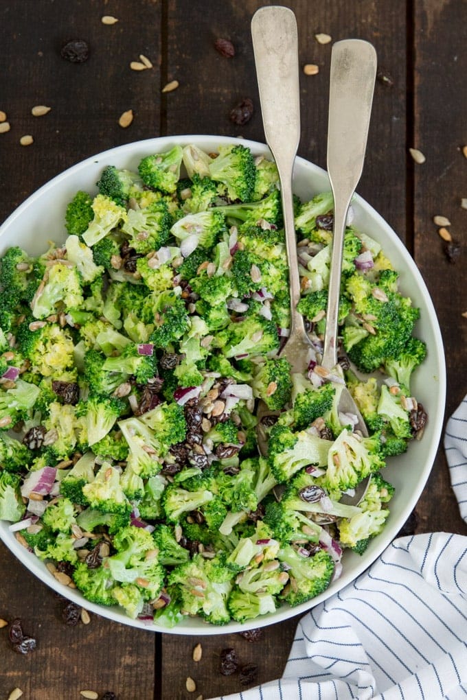 An overhead shot of broccoli salad in a white bowl with two salad spoons.