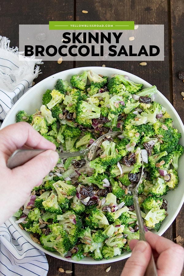 Broccoli Salad in a large bowl, being tossed with silver spoons.