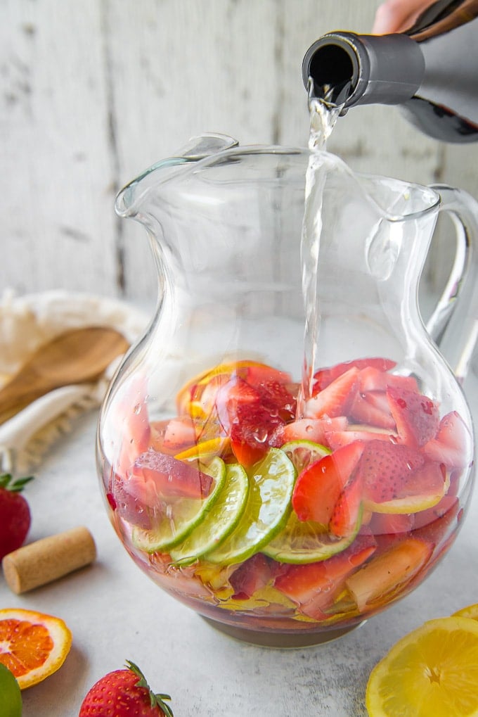 Pouring wine into a large pitcher filled with fruit