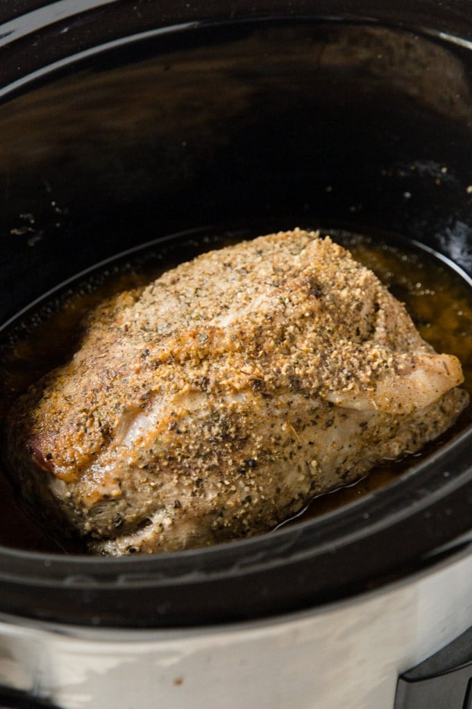 A seasoned pork roast, whole, in a slow cooker