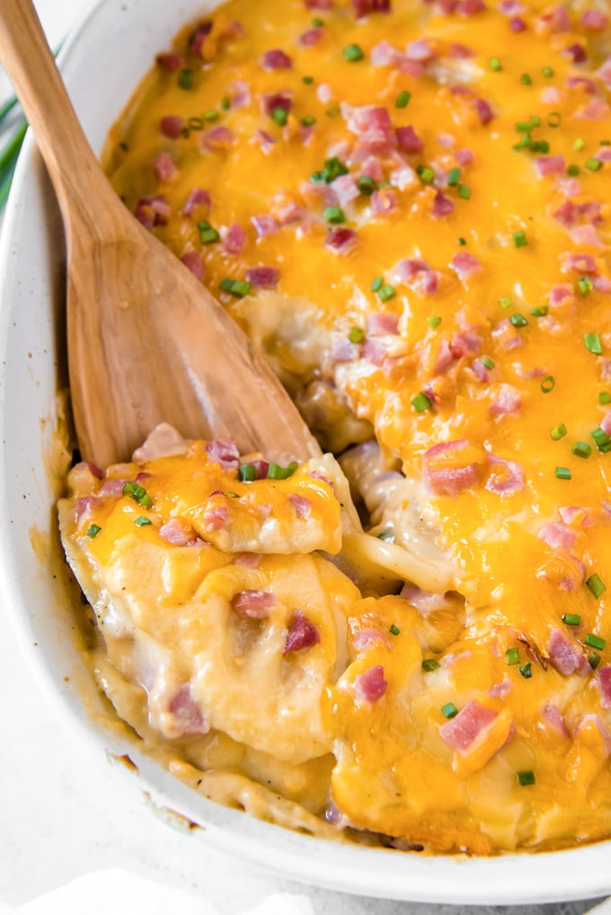 A wooden spoon digging into to this cheesy ham and potato casserole