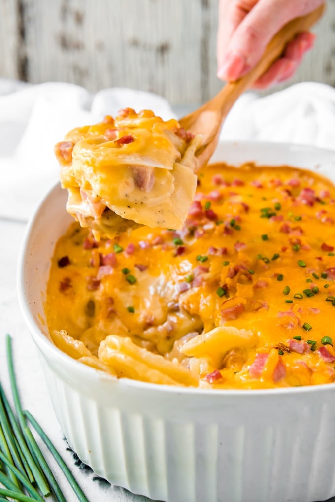 A wooden spoon with a serving of potato and ham casserole