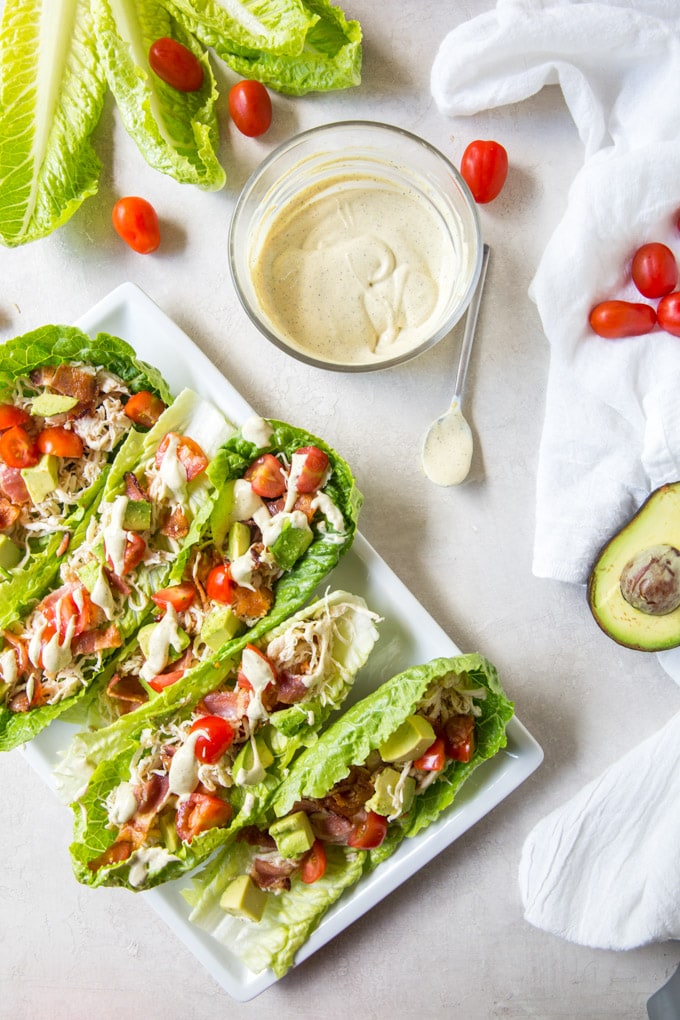 Chicken Club lettuce wraps on a plate, a bowl of dressing and tomatoes