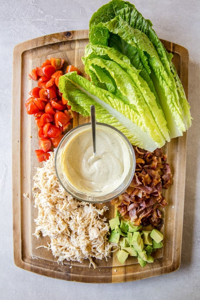 Ingredients to make lettuce wraps - Lettuce leaves, diced tomatoes, shredded chicken, bacon and avocado on a cutting board